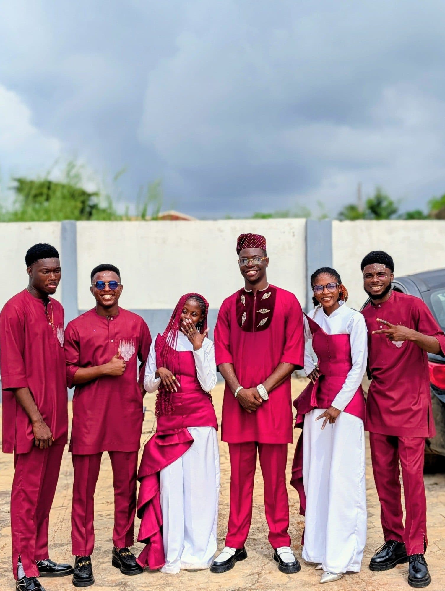 Six smiling members in matching burgundy and white outfits standing together outdoors